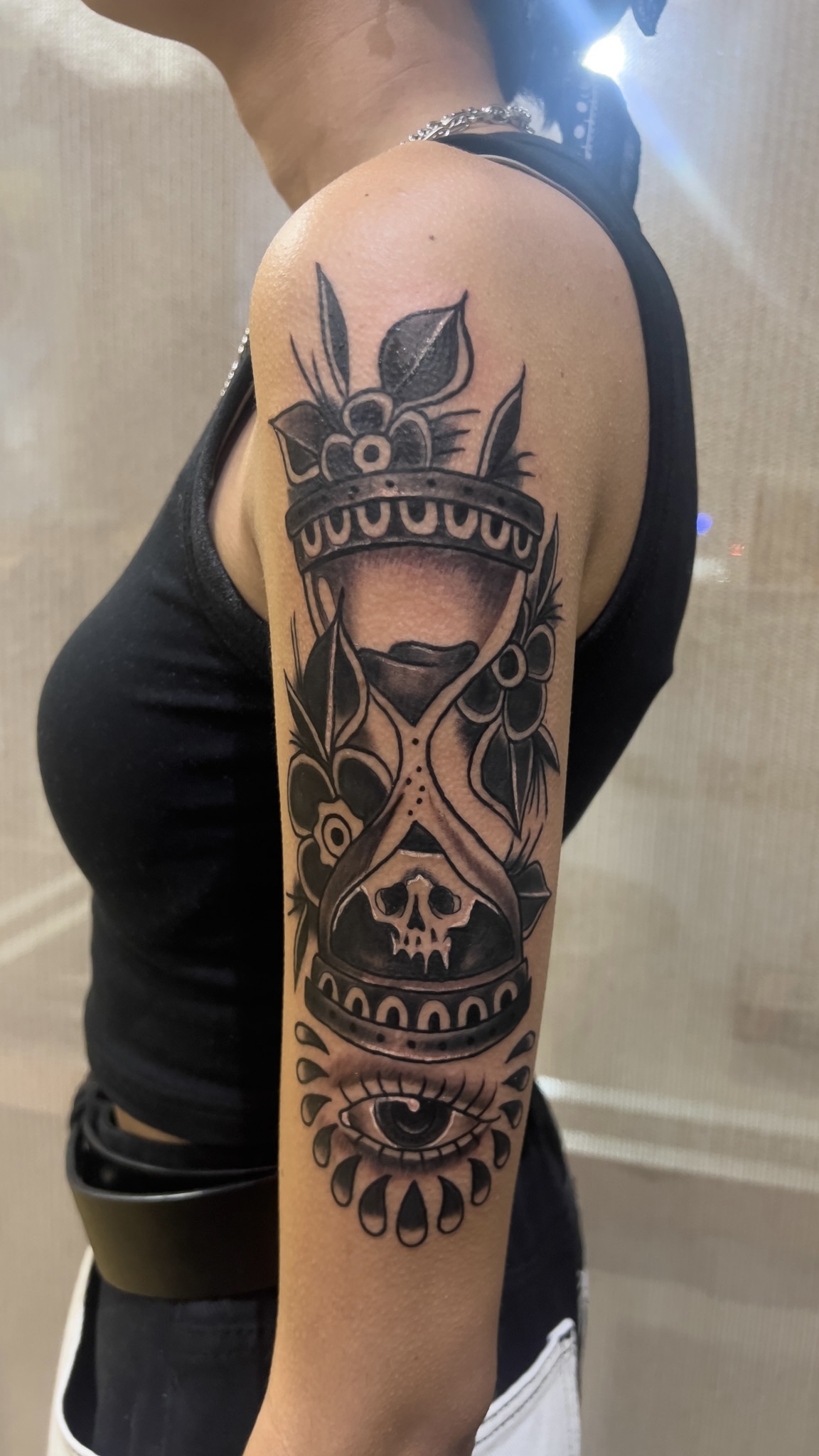 Black and grey hourglass with skull and all-seeing eye upper arm tattoo